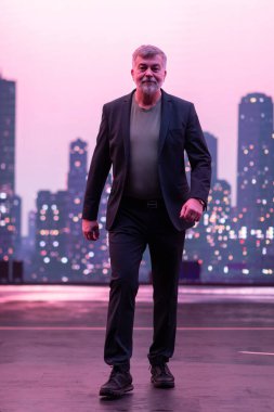 Şık takım elbiseli kendinden emin bir üst sınıf öğrencisi alacakaranlıkta parlayan şehir siluetine karşı kameraya doğru yürüyor.. 