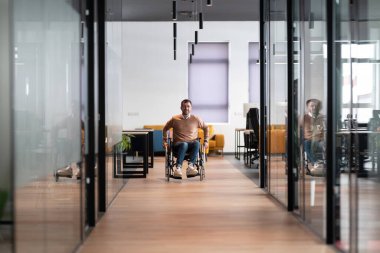 Tekerlekli sandalyede bir adamın olduğu cam duvarları olan modern bir ofis koridoru. Uzay, parlak tasarımı ve parlak ışıklandırması olan, kapsayıcı, erişilebilir bir iş yeri sergiliyor..