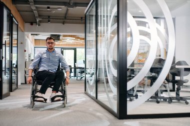 Büyük, modern bir şirkette, tekerlekli sandalyedeki kararlı bir işadamı bir koridorda dolaşır, kurumsal dünyaya güç ve kapsayıcılık kazandırır.