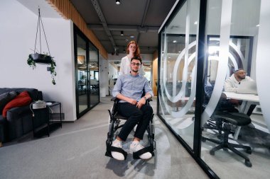 İş arkadaşları, işbirlikçi iş arkadaşları, tekerlekli sandalyedeki bir kişi de dahil olmak üzere, iş yerlerindeki çeşitliliği, takım çalışmasını ve yetkilendirmeyi gösteren modern cam ofis koridorunun yanından geçtiler.