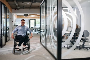 Büyük, modern bir şirkette, tekerlekli sandalyedeki kararlı bir işadamı bir koridorda dolaşır, kurumsal dünyaya güç ve kapsayıcılık kazandırır.