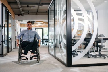 Büyük, modern bir şirkette, tekerlekli sandalyedeki kararlı bir işadamı bir koridorda dolaşır, kurumsal dünyaya güç ve kapsayıcılık kazandırır.