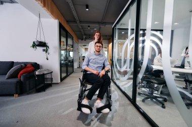 İş arkadaşları, işbirlikçi iş arkadaşları, tekerlekli sandalyedeki bir kişi de dahil olmak üzere, iş yerlerindeki çeşitliliği, takım çalışmasını ve yetkilendirmeyi gösteren modern cam ofis koridorunun yanından geçtiler.