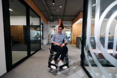 İş arkadaşları, işbirlikçi iş arkadaşları, tekerlekli sandalyedeki bir kişi de dahil olmak üzere, iş yerlerindeki çeşitliliği, takım çalışmasını ve yetkilendirmeyi gösteren modern cam ofis koridorunun yanından geçtiler.