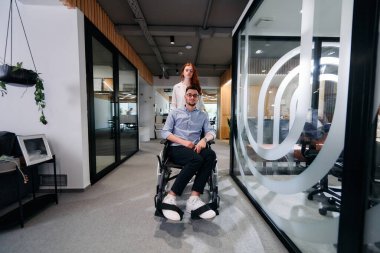 İş arkadaşları, işbirlikçi iş arkadaşları, tekerlekli sandalyedeki bir kişi de dahil olmak üzere, iş yerlerindeki çeşitliliği, takım çalışmasını ve yetkilendirmeyi gösteren modern cam ofis koridorunun yanından geçtiler.