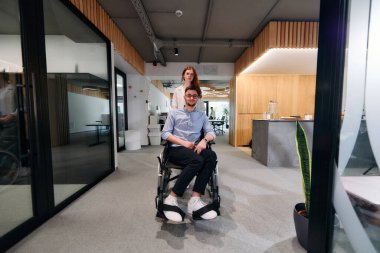 İş arkadaşları, işbirlikçi iş arkadaşları, tekerlekli sandalyedeki bir kişi de dahil olmak üzere, iş yerlerindeki çeşitliliği, takım çalışmasını ve yetkilendirmeyi gösteren modern cam ofis koridorunun yanından geçtiler.