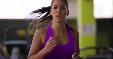 Pembe spor kıyafetli genç bir kadın modern bir spor salonunda koşu bandında koşuyor, kilo vermeye, dayanıklılığı artırmaya ve selüliti azaltmaya odaklanıyor. Formda kalma hedeflerine kendini adamış durumda.