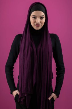 Başörtülü çarpıcı bir Müslüman kadın zarif bir şekilde stüdyoda pembe bir arka plana karşı poz veriyor, zarafet ve güven yayıyor.. 