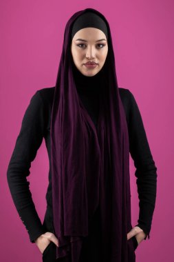 Başörtülü çarpıcı bir Müslüman kadın zarif bir şekilde stüdyoda pembe bir arka plana karşı poz veriyor, zarafet ve güven yayıyor..