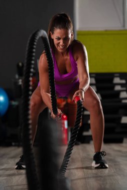 Formda ve atletik bir kadın spor salonunda halatla koşma egzersizleri yapar. Gücünü, dayanıklılığını ve kendini spora adamışlığını gösterir.. 