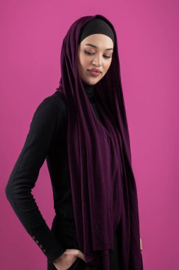 Başörtülü çarpıcı bir Müslüman kadın zarif bir şekilde stüdyoda pembe bir arka plana karşı poz veriyor, zarafet ve güven yayıyor.. 