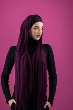 Başörtülü çarpıcı bir Müslüman kadın zarif bir şekilde stüdyoda pembe bir arka plana karşı poz veriyor, zarafet ve güven yayıyor.. 