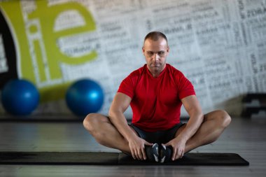 A fitness man stretches in the gym after an intense workout, focusing on recovery and flexibility clipart