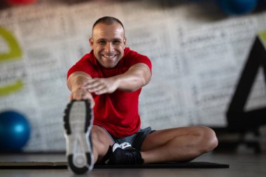 A fitness man stretches in the gym after an intense workout, focusing on recovery and flexibility clipart