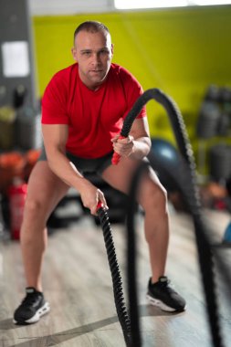 Kararlı bir adam, spor salonundaki savaş halatlarıyla yoğun kardiyo egzersizleri yaparken limitlerini zorlar. Gücünü, dayanıklılığını gösterir ve odaklanır.. 