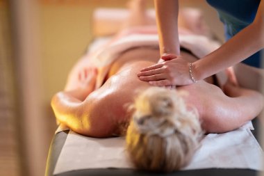 Spa 'da Sırt Masajı. Mavi üniformalı profesyonel bir masaj terapisti masaj masasında yatan bir müşteriye rahatlatıcı bir sırt masajı sağlar.