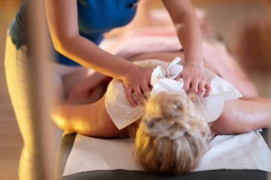 Spa 'da Sırt Masajı. Mavi üniformalı profesyonel bir masaj terapisti masaj masasında yatan bir müşteriye rahatlatıcı bir sırt masajı sağlar.