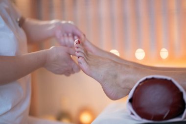 Beyaz üniformalı profesyonel bir masaj terapisti, sakin ve sakin bir spa ortamında müşteriye rahatlatıcı bir ayak masajı sağlar..
