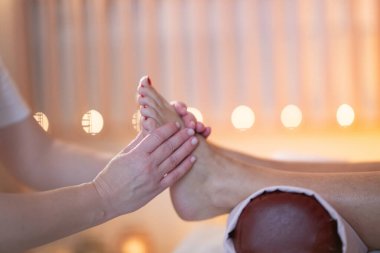 Beyaz üniformalı profesyonel bir masaj terapisti, sakin ve sakin bir spa ortamında müşteriye rahatlatıcı bir ayak masajı sağlar..