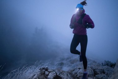 Geceleri engebeli dağ arazisinde koşan bir kadın patikası, bir far ışığıyla aydınlatılan yolu.