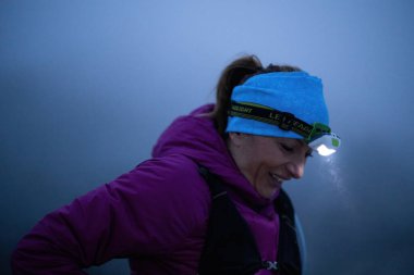 Geceleri engebeli dağ arazisinde koşan bir kadın patikası, bir far ışığıyla aydınlatılan yolu.