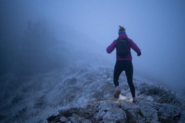 Geceleri engebeli dağ arazisinde koşan bir kadın patikası, bir far ışığıyla aydınlatılan yolu.