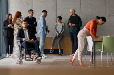 Modern bir ofiste, iş dünyasından çeşitli profesyonellerden oluşan bir ekip, yönetmenlerinin yanında duruyor. Tekerlekli sandalyede, işe dahil olma, işbirliği ve liderliğin simgesi olarak.. 