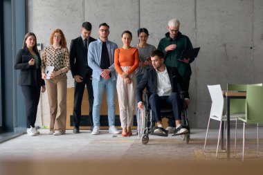 Çağdaş bir ofiste tekerlekli sandalyede müdürle işbirliği yapan çok ırklı iş adamları..