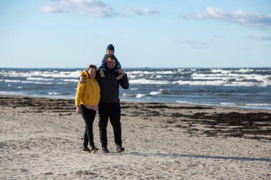 Mutlu bir aile, serin bir sonbahar plajı boyunca yürür. Genç oğulları sevinçle koşar, taze rüzgar ve dindirici dalgalar onları bir anda kucaklarken kalıcı anılar yaratır.