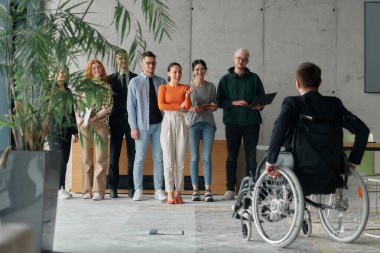 Çağdaş bir ofiste tekerlekli sandalyede müdürle işbirliği yapan çok ırklı iş adamları..