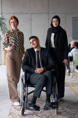 Çeşitli bir iş ekibi güven içinde poz veriyor. Aralarında tekerlekli sandalyede oturan gülümseyen bir yönetmen de var. Birinde tesettür takan, diğerinde tablet tutan iki profesyonel meslektaşı var.