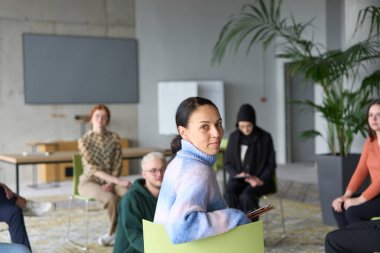 Çeşitli iş adamları modern bir ofiste dikkatle oturup, bir eğitmenin önderliğindeki bir eğitim oturumunda aktif olarak en son teknolojik gelişmelere odaklanırlar.