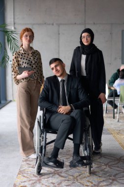 Çeşitli bir iş ekibi güven içinde poz veriyor. Aralarında tekerlekli sandalyede oturan gülümseyen bir yönetmen de var. Birinde tesettür takan, diğerinde tablet tutan iki profesyonel meslektaşı var.
