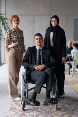 Çeşitli bir iş ekibi güven içinde poz veriyor. Aralarında tekerlekli sandalyede oturan gülümseyen bir yönetmen de var. Birinde tesettür takan, diğerinde tablet tutan iki profesyonel meslektaşı var.