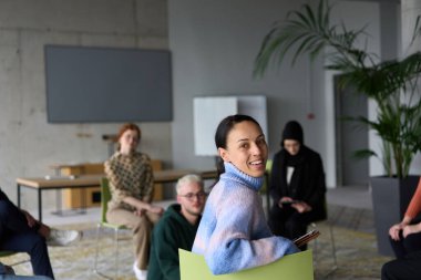 Çeşitli iş adamları modern bir ofiste dikkatle oturup, bir eğitmenin önderliğindeki bir eğitim oturumunda aktif olarak en son teknolojik gelişmelere odaklanırlar.
