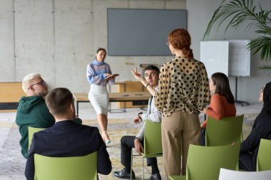 Çeşitli iş adamları modern bir ofiste dikkatle oturup, bir eğitmenin önderliğindeki bir eğitim oturumunda aktif olarak en son teknolojik gelişmelere odaklanırlar.