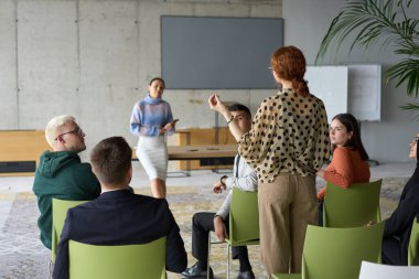 Çeşitli iş adamları modern bir ofiste dikkatle oturup, bir eğitmenin önderliğindeki bir eğitim oturumunda aktif olarak en son teknolojik gelişmelere odaklanırlar.
