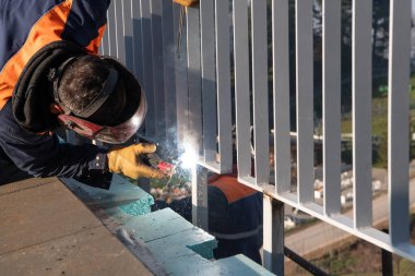 Endüstriyel kaynakçı yeni bir işletme kompleksi için metal çit ustalıkla hazırlıyor, modern ekipmanlar kullanarak, parlak kıvılcımlar saçıyor ve zanaatın hassasiyetini ve adanmışlığını vurguluyor.