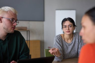 Genç, çeşitli bir iş ekibi modern bir ofiste birlikte oturuyor, fikir ve iş planlarını paylaşıyor, gelecekteki başarı için işbirliği ve yenilikleri teşvik ediyor.