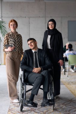 Çeşitli bir iş ekibi güven içinde poz veriyor. Aralarında tekerlekli sandalyede oturan gülümseyen bir yönetmen de var. Birinde tesettür takan, diğerinde tablet tutan iki profesyonel meslektaşı var.