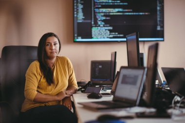Bilgisayarlarla çevrili bir programcı ofisinde oturan bir iş kadını uzmanlığını ve teknolojiye olan bağlılığını gösteriyor.