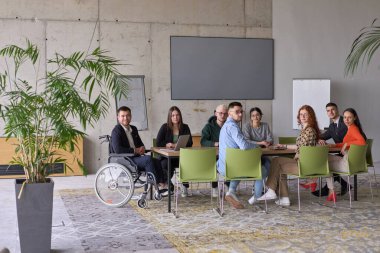 Muhtelif bir grup iş adamı, yöneticileriyle bir ofiste oturuyorlar, şu anda tekerlekli sandalyede, işbirliği, liderlik ve kapsayıcılığı destekliyorlar..