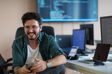 Bir programcı ofisinde otururken akıllı telefon uygulamalarını özenle test eder.