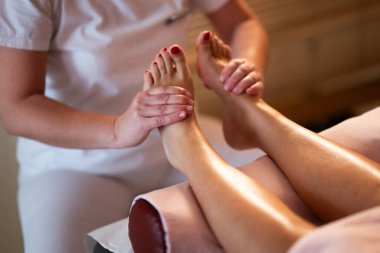 Beyaz üniformalı profesyonel bir masaj terapisti, sakin ve sakin bir spa ortamında müşteriye rahatlatıcı bir ayak masajı sağlar..