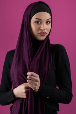 Başörtülü çarpıcı bir Müslüman kadın zarif bir şekilde stüdyoda pembe bir arka plana karşı poz veriyor, zarafet ve güven yayıyor..