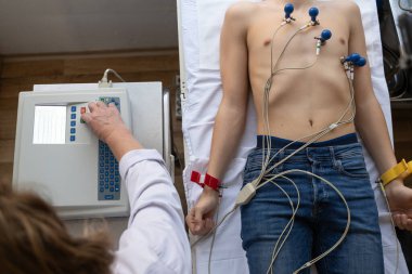 Kadın bir doktor, hastane odasında genç bir adama EKG çeker. Rutin bir kontrol sırasında kalp sağlığını dikkatle izler.