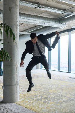 Modern bir ofise kendinden geçmiş bir şekilde atlayan bir işadamı, elinde bir evrak çantasıyla, başarı ve zafer anını kutluyor.