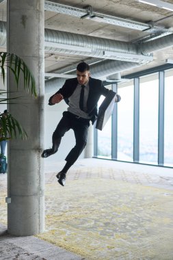 Modern bir ofise kendinden geçmiş bir şekilde atlayan bir işadamı, elinde bir evrak çantasıyla, başarı ve zafer anını kutluyor.