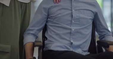 Genç iş arkadaşları, işbirlikçi iş arkadaşları, aralarında tekerlekli sandalyedeki bir kişinin de bulunduğu, modern cam ofis koridorunun yanından geçerek, çeşitliliği, takım çalışmasını ve güçlendirmeyi resmediyorlar.