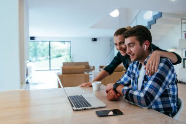 Genç evli bir çift, modern evlerinin oturma odasında otururken bir dizüstü bilgisayarla ebeveynleri, aileleri ve arkadaşlarıyla konuşuyor.